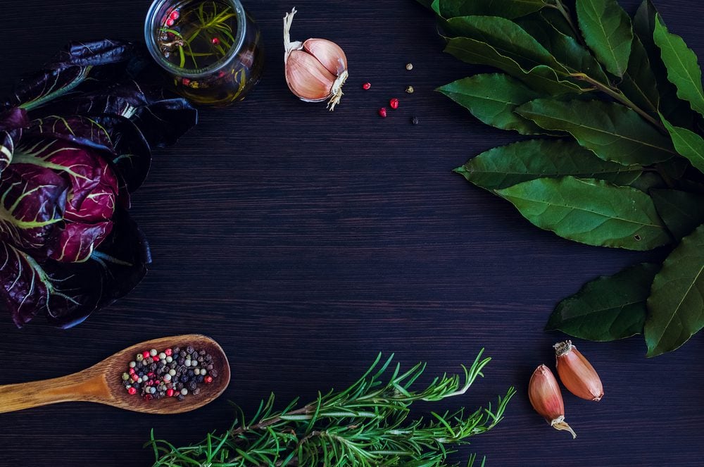 Garlic, chicory, rosemary, and bay leaves on a dark-colored table